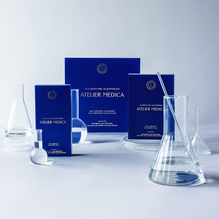 Blue Clementine Sleepwear Atelier Medica product boxes with clear glass lab beakers and flasks on white background - #color_pearl-white