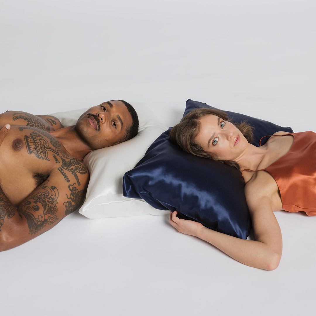 Man with chest tattoos resting on a pearl-white pillow beside a woman lying on a navy silk pillow - #color_pearl-white