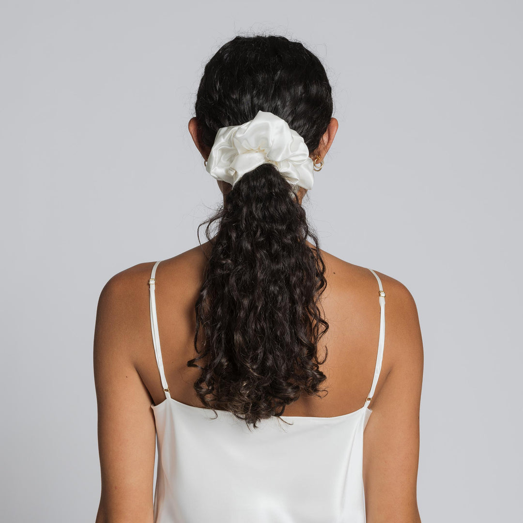 White silk scrunchie holding dark curly ponytail at nape