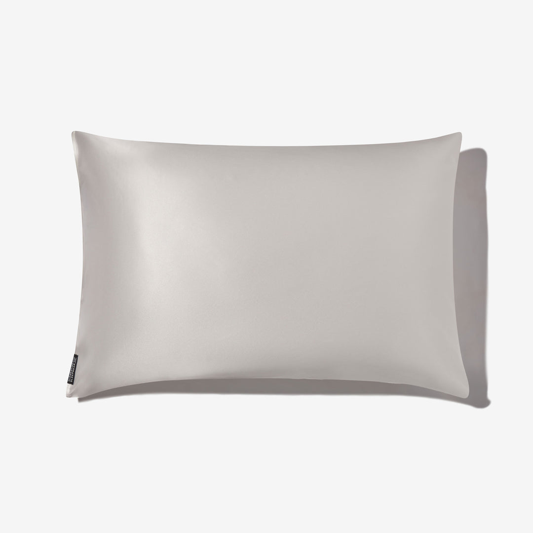 Pearl-white pillow with subtle silk sheen, rectangular shape, small black side tag at bottom-left, soft shadow to the right. - #color_pearl-white