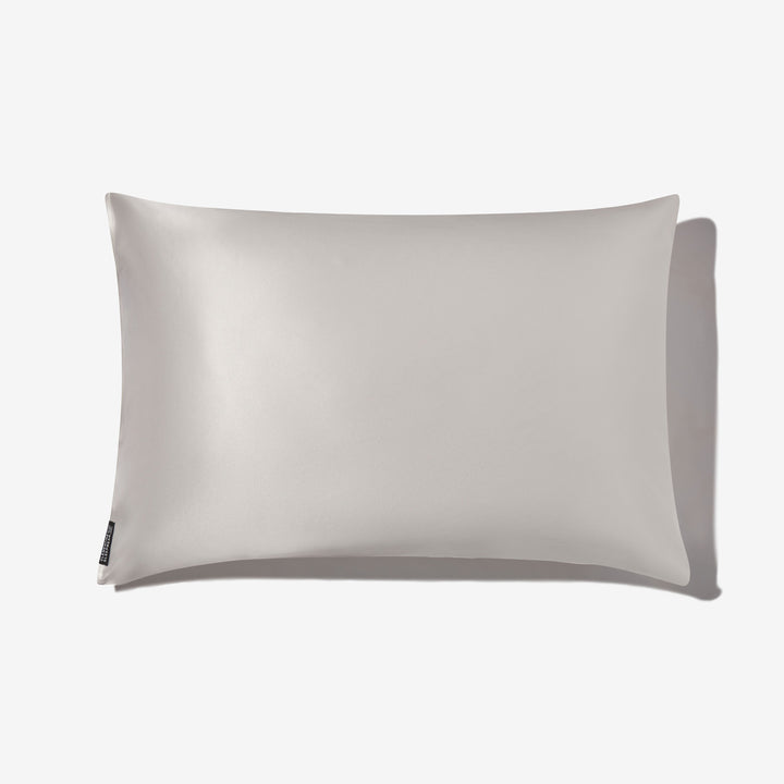 Pearl-white pillow with subtle silk sheen, rectangular shape, small black side tag at bottom-left, soft shadow to the right. - #color_pearl-white