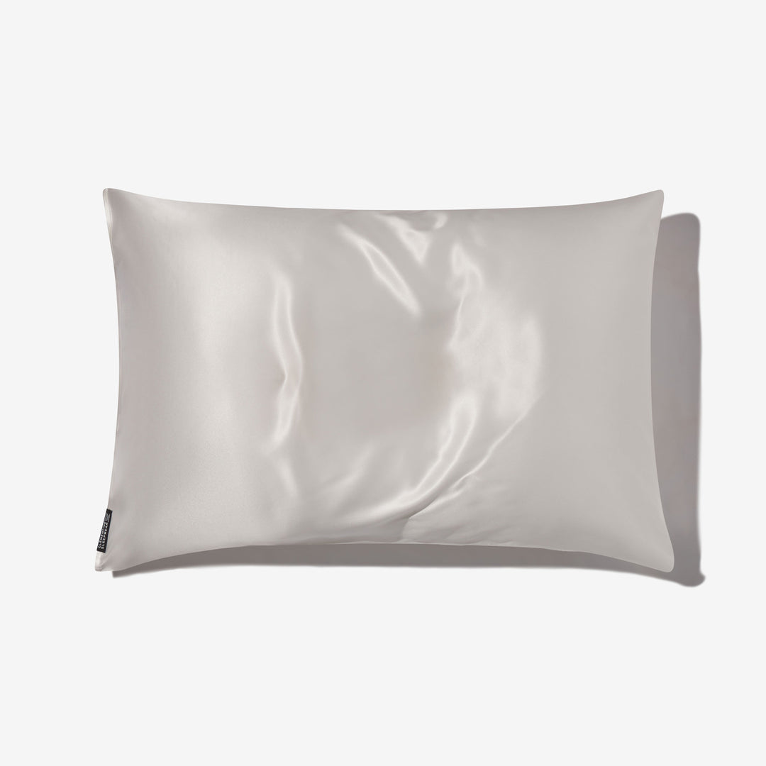 Pearl-white silk pillowcase with glossy sheen, flat on white background, small fabric care tag at lower left. - #color_pearl-white