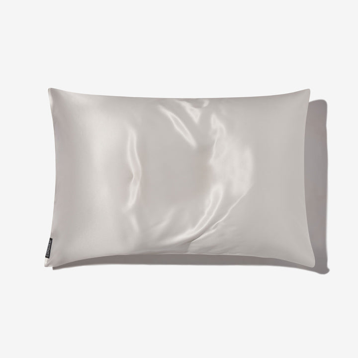 Pearl-white silk pillowcase with glossy sheen, flat on white background, small fabric care tag at lower left. - #color_pearl-white