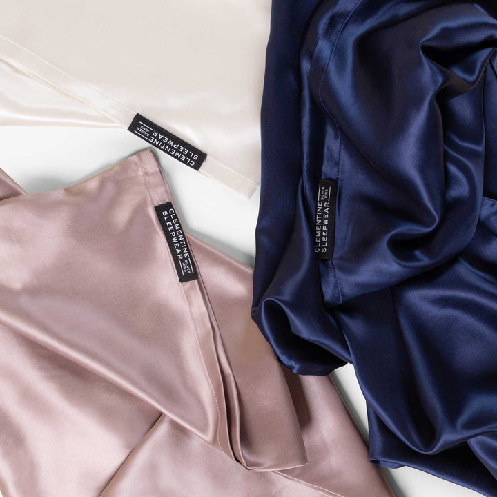 Three silk sleepwear pieces in mauve, white, and navy blue with labels 'CLEMENTINE SLEEPWEAR SILVER IONS' - #color_navy-blue