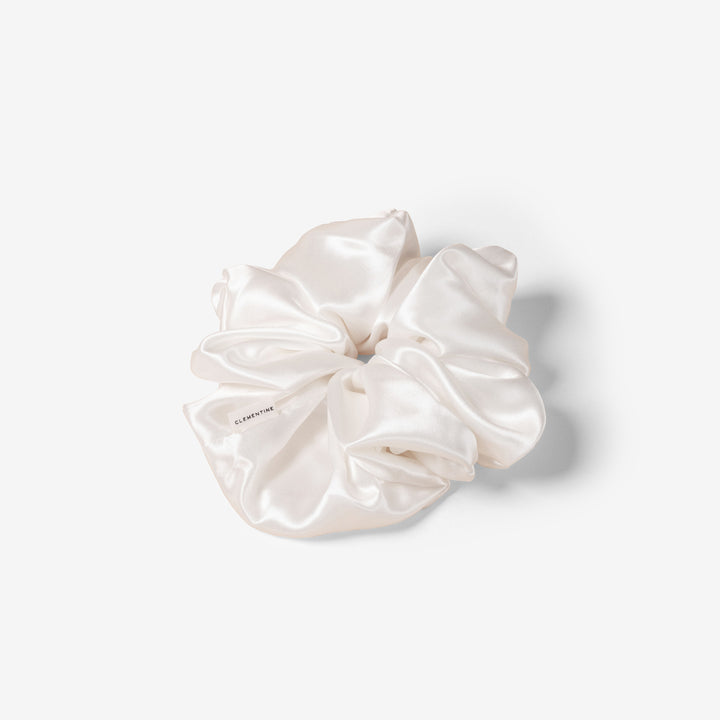 White silk scrunchie with CLEMENTINE label, close-up showing satin sheen and gathered folds.