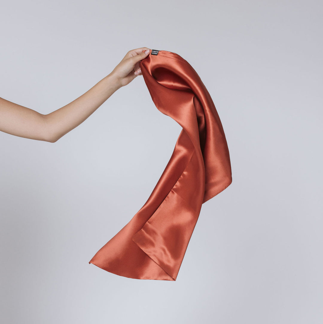 Hand holding a dusk maroon satin pillowcase with black tag reading Clementine, fabric draping#color_dusk