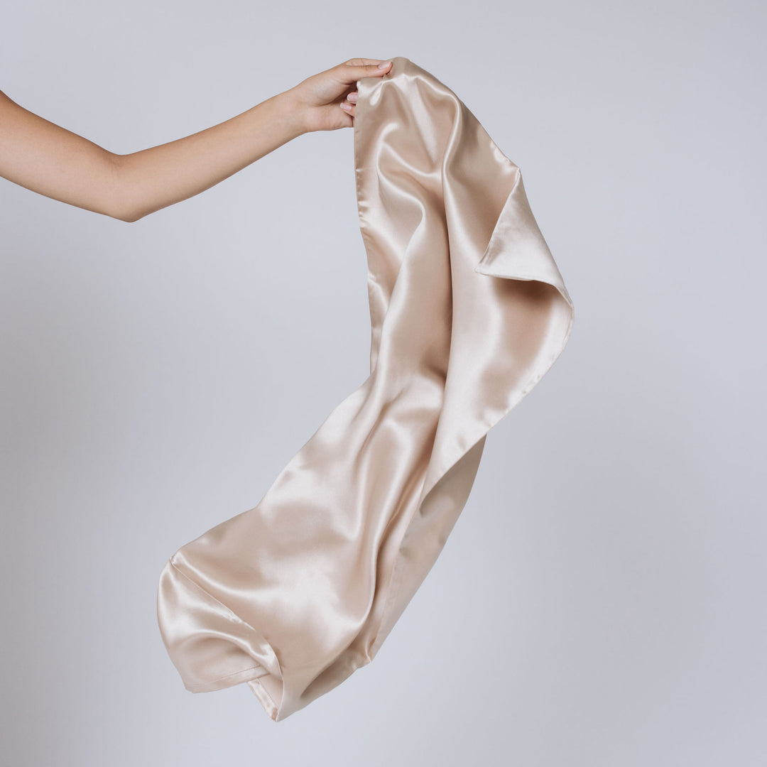 Champagne-gold satin pillowcase held by hand against a plain light background - #color_champagne-gold
