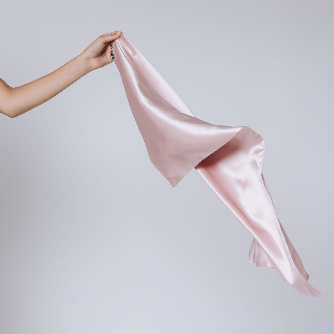 Left hand holding a pale pink silk pillowcase, draped to show smooth sheen and flowing folds - hand holding pink pillowcase#color_pink-sherbert