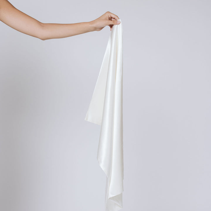 Arm holding a pearl-white silk pillowcase draped to show its sheen and fabric texture#color_pearl-white