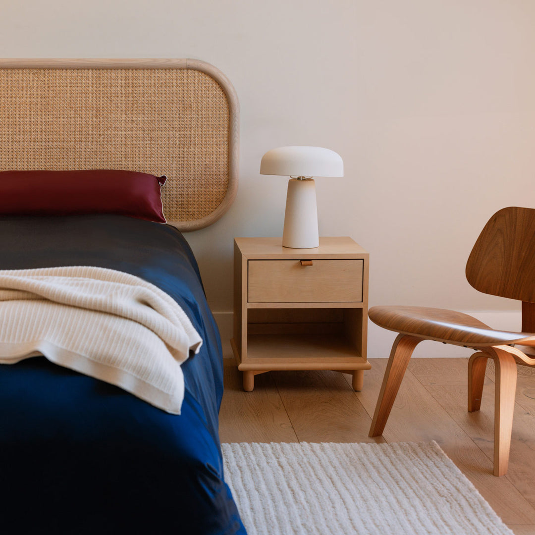 Bedroom corner with navy blue bedspread, wooden nightstand with white lamp, and wooden chair on light floor rug. - #color_navy-blue