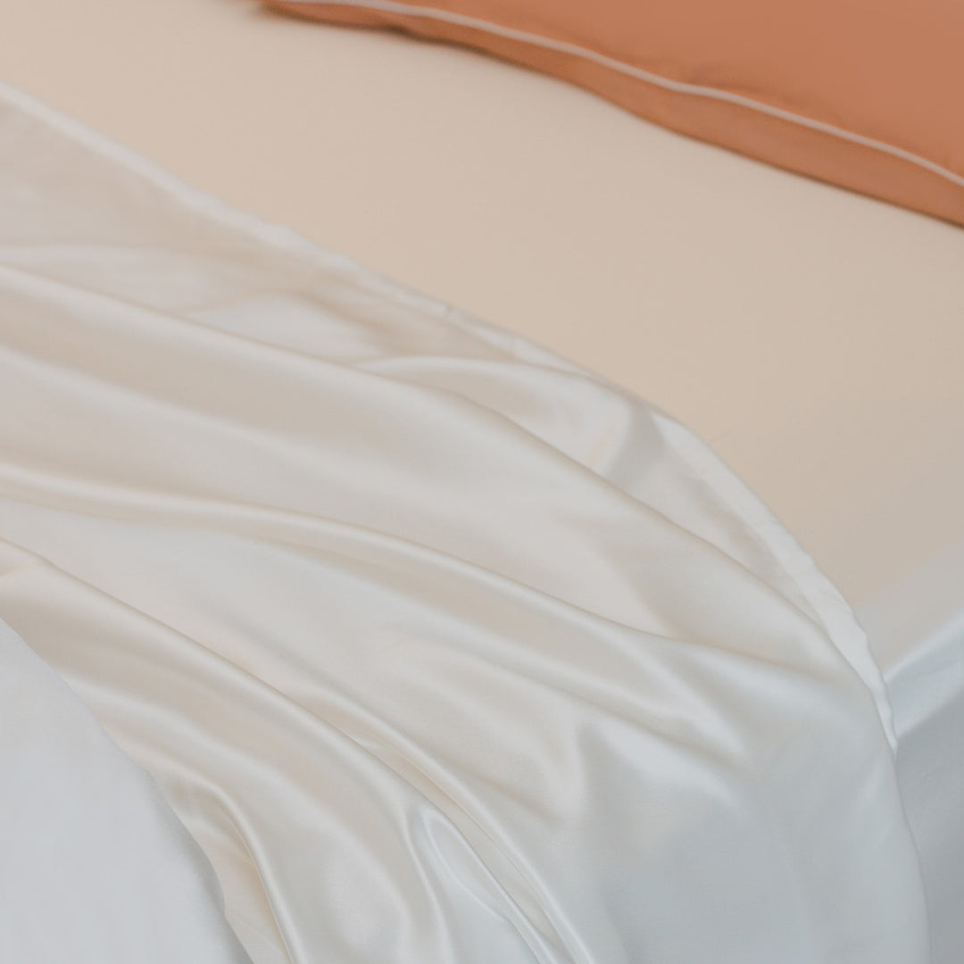 Ivory organic silk fitted sheet draped over a mattress corner