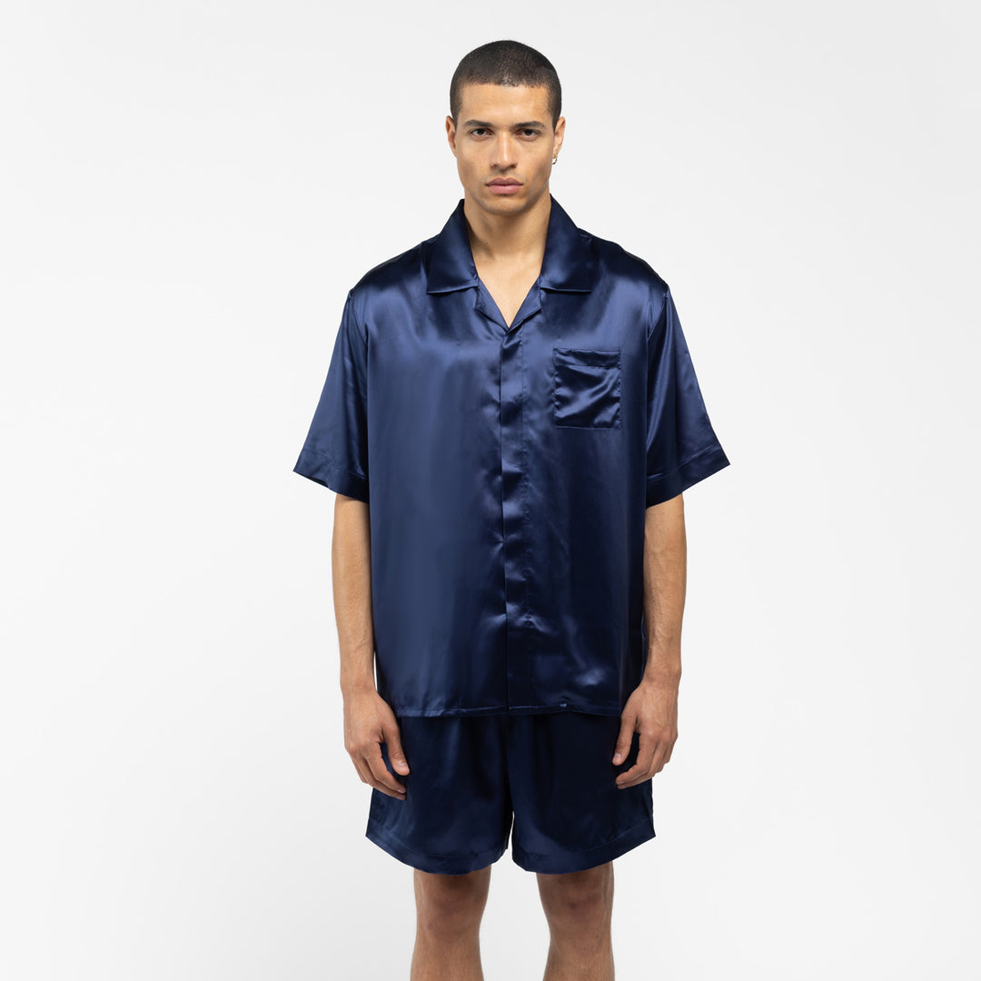 Man wearing navy blue silk short-sleeve shirt and matching shorts, standing against white background - #color_navy-blue