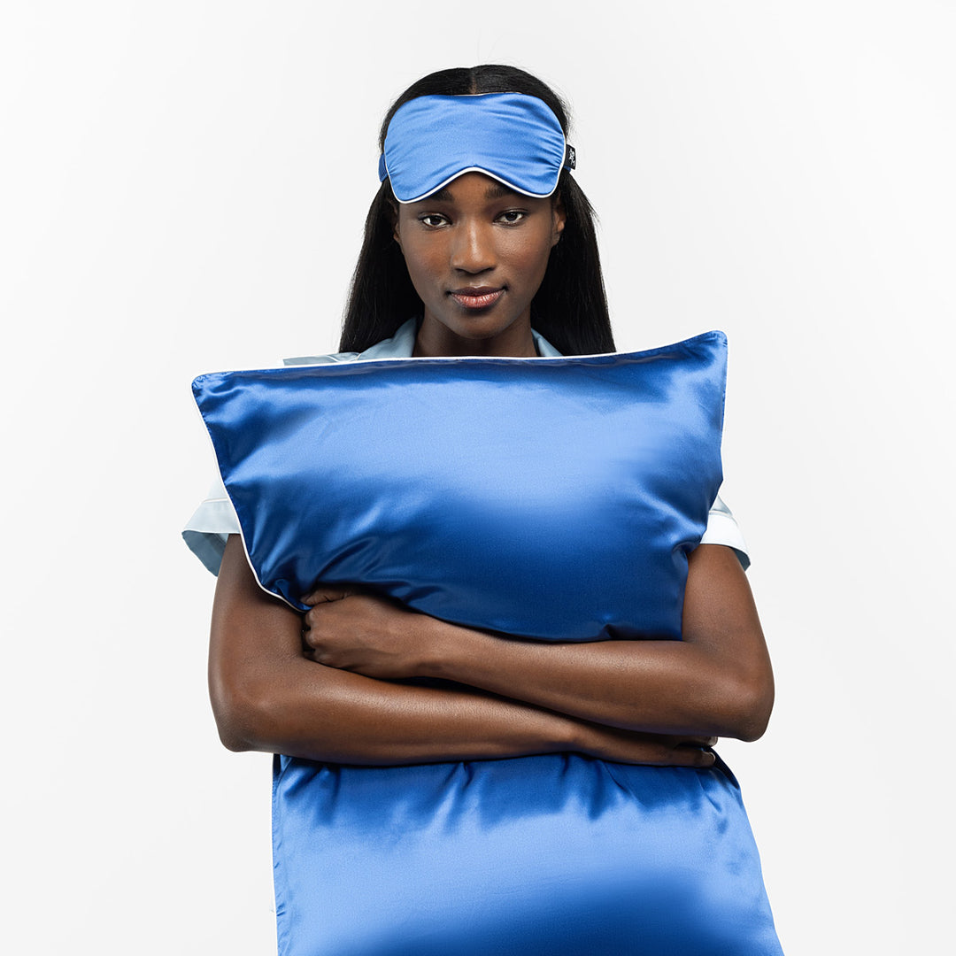 Woman holding a blue silk pillow and wearing a matching blue sleep mask - #color_ocean