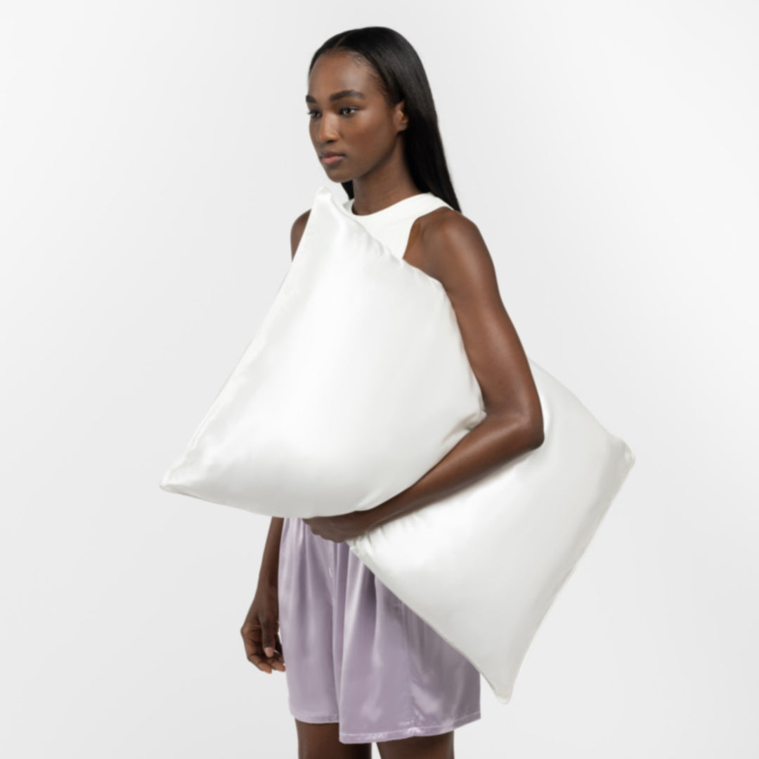 Woman holding two large pearl-white pillows, wearing a white top and lavender shorts. - #color_pearl-white