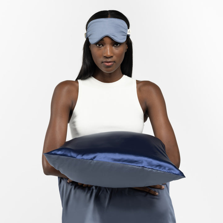 Woman holding a navy silk pillow, wearing a light blue sleep mask and white sleeveless top - #color_blue-lagoon
