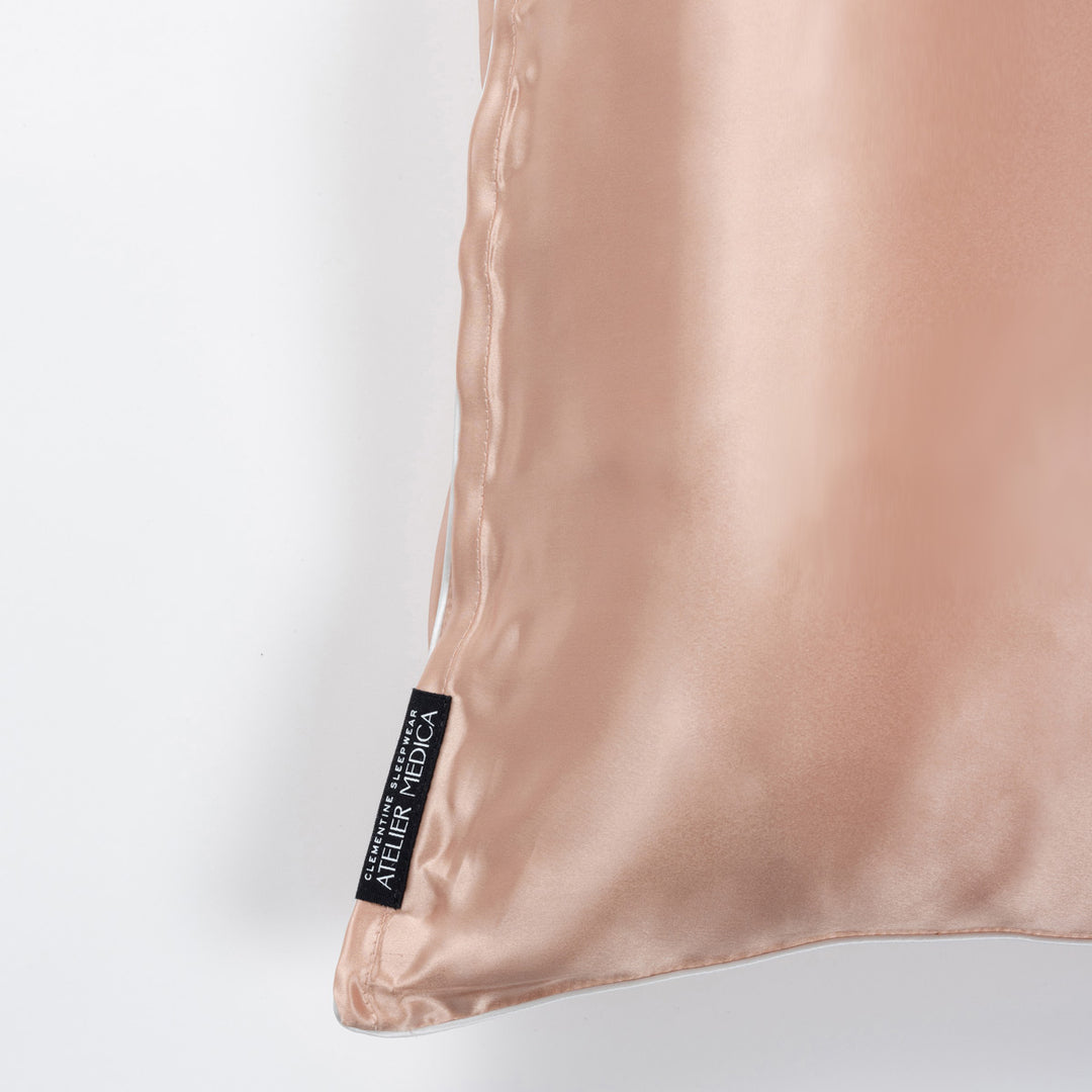 Corner of clementine-peach silk pillowcase showing black tag reading ATELIER MEDICA - #color_clementine-peach