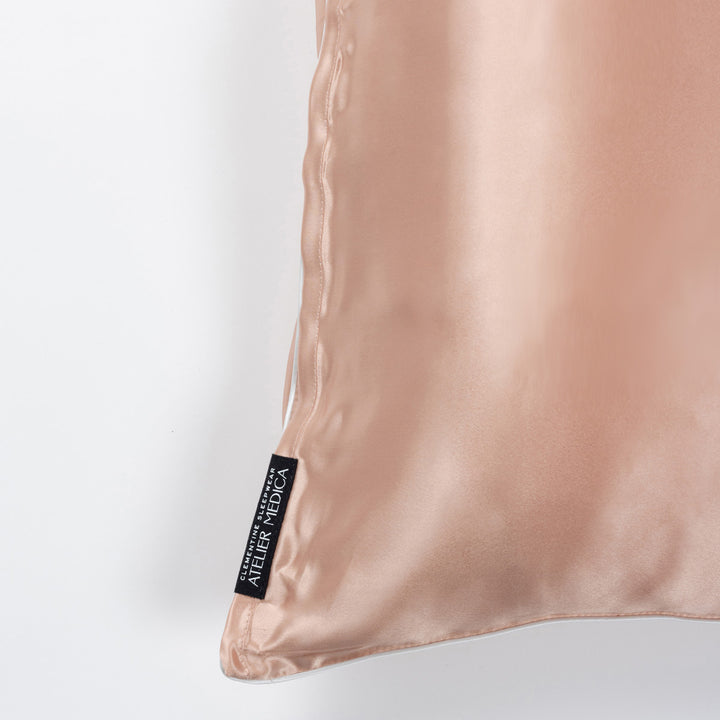 Corner of clementine-peach silk pillowcase showing black tag reading ATELIER MEDICA - #color_clementine-peach