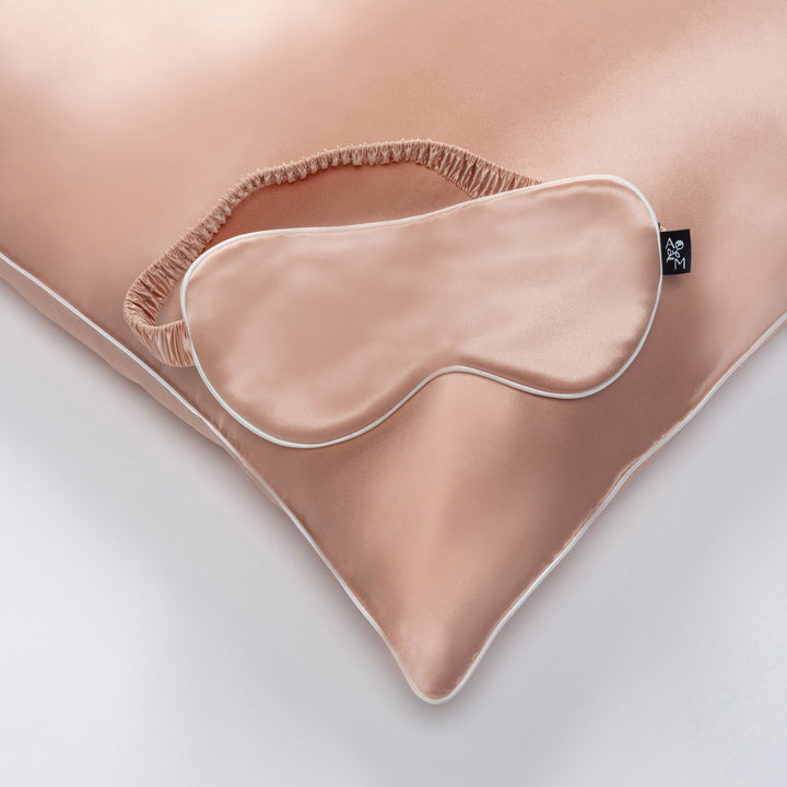 Silk sleep mask on matching pillow, clementine-peach color, black tag reading 'AEM' - #color_clementine-peach