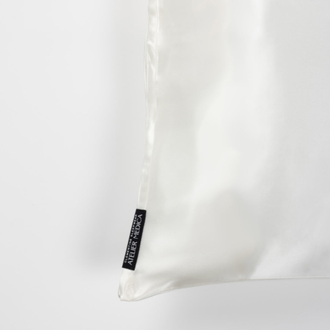 Pearl-white silk pillowcase corner with black brand tag reading 'ATELIER MEDICA'. - #color_pearl-white