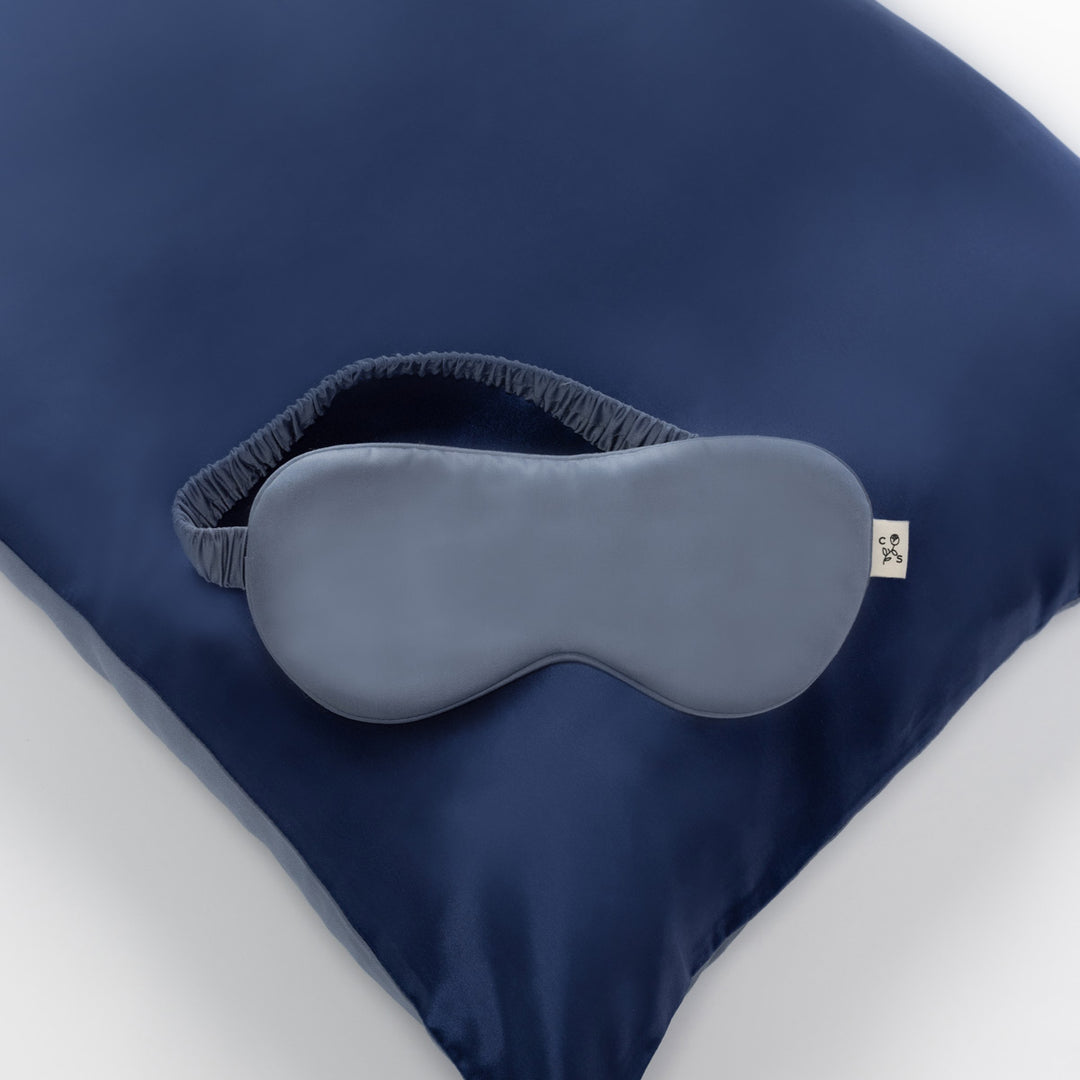 navy silk pillow topped with a gray silk sleep mask with elastic strap - #color_blue-lagoon
