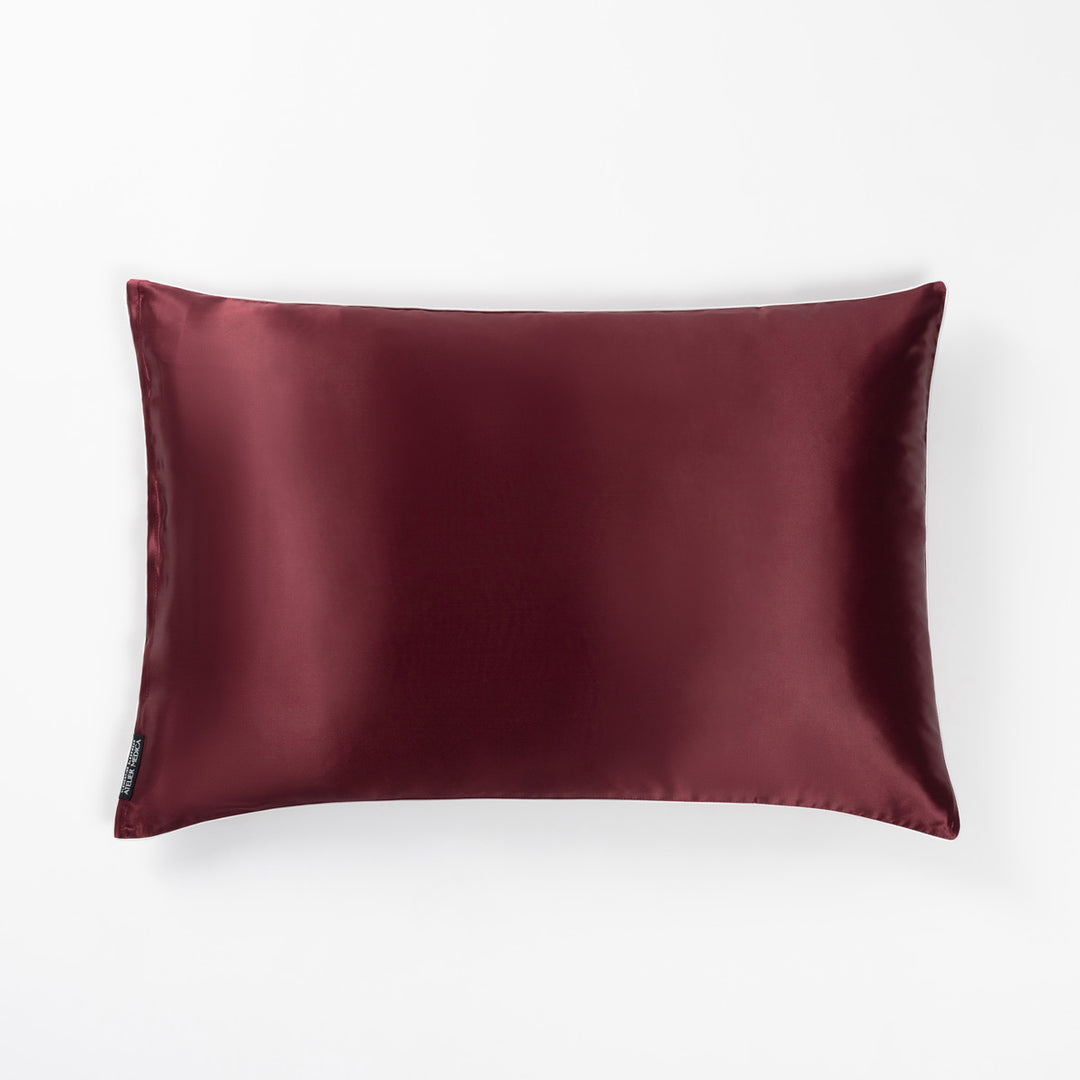 Plum-colored rectangular silk pillow with a small black tag on the side - #color_plum