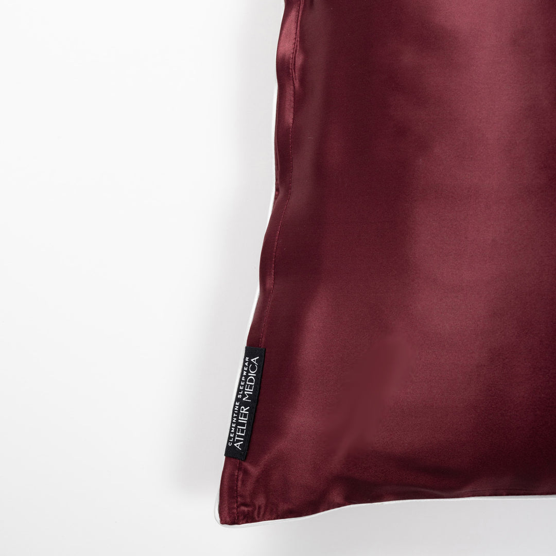 Plum silk pillowcase corner with black woven label reading 'ATELIER MEDICA' - #color_plum