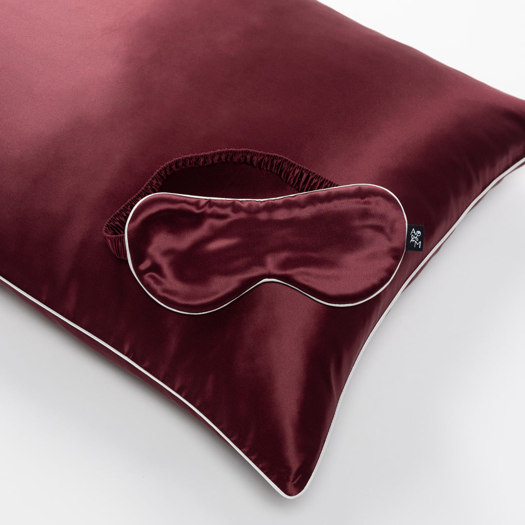 Plum-colored silk pillow with matching sleep mask and white piping detail - #color_plum