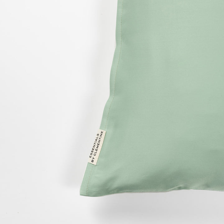 Corner of mint-green pillowcase with sewn tag reading ESSENTIALS BY CLEMENTINE.