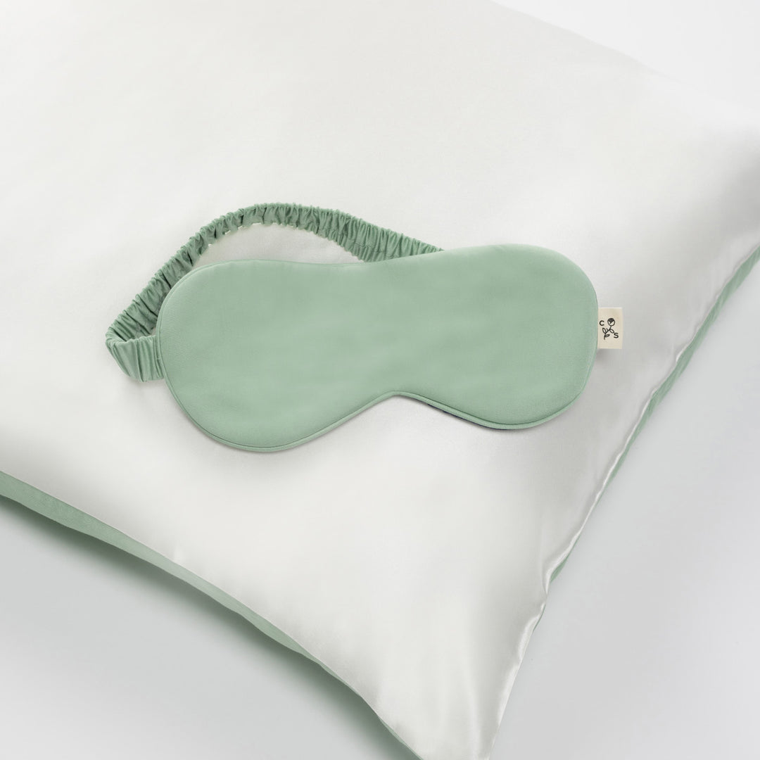 Mint green silk sleep mask on a white silk pillow, elastic ruched strap visible - #color_match-point-green