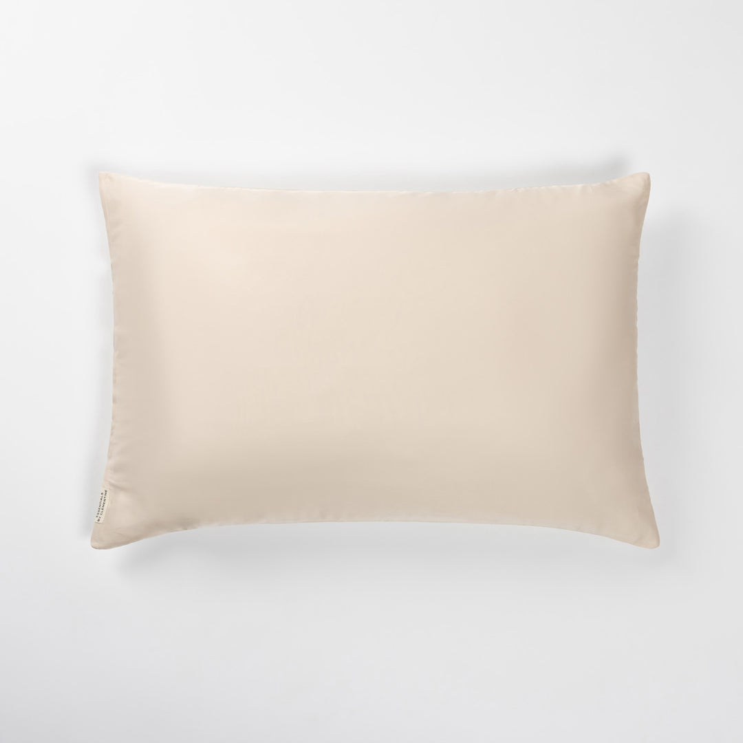 Champagne-colored rectangular pillow with welted edges and small sewn care tag at lower-left. - #color_champagne-sunset