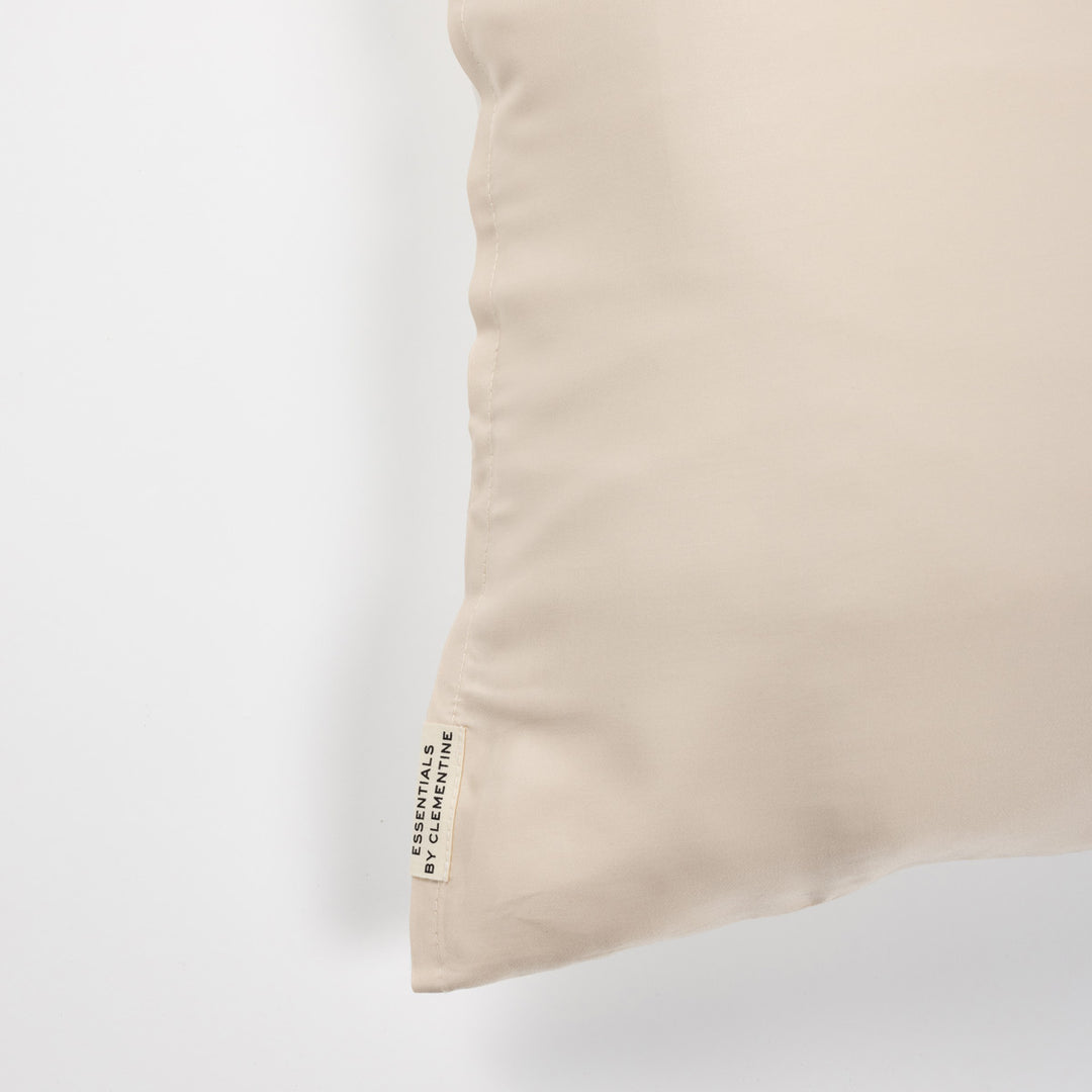 Champagne-colored pillow corner with fabric tag reading ESSENTIALS BY CLEMENTINE - #color_champagne-sunset
