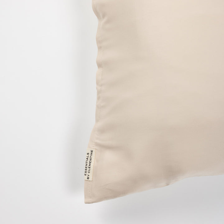 Champagne-colored pillow corner with fabric tag reading ESSENTIALS BY CLEMENTINE - #color_champagne-sunset