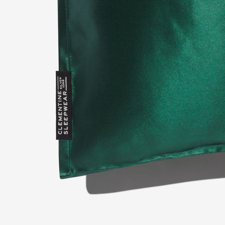 Forest-green silk pillowcase corner with black tag reading 'CLEMENTINE SLEEPWEAR' and small text 'SILVER IONS' - Pillowcase green corner#color_forest-green