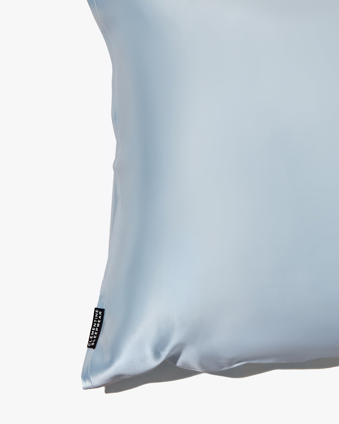 Close-up of a blue silk pillowcase with a subtle texture and a brand label visible on the edge.