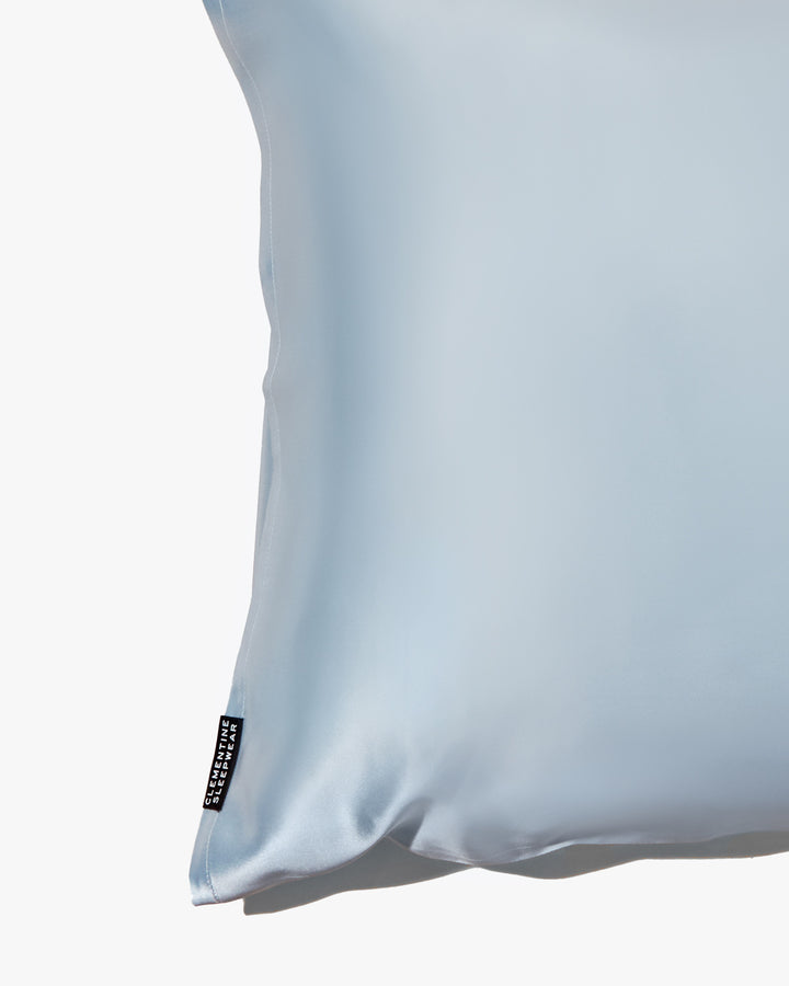 Close-up of a blue silk pillowcase with a subtle texture and a brand label visible on the edge.