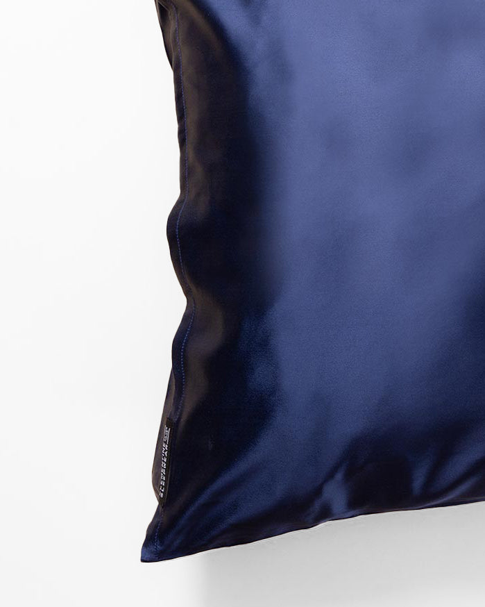 Close-up of a dark blue satin pillow with a small fabric tag on the side.