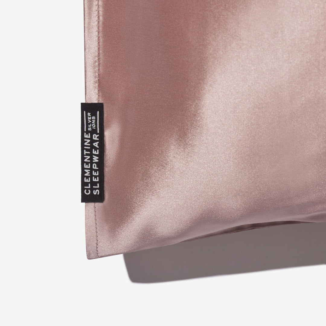 Rose-mist silk pillowcase corner with black tag reading 'CLEMENTINE SLEEPWEAR SILVER IONS' - #color_rose-mist