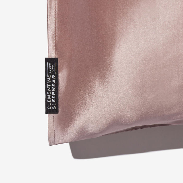 Rose-mist silk pillowcase corner with black tag reading 'CLEMENTINE SLEEPWEAR SILVER IONS' - #color_rose-mist