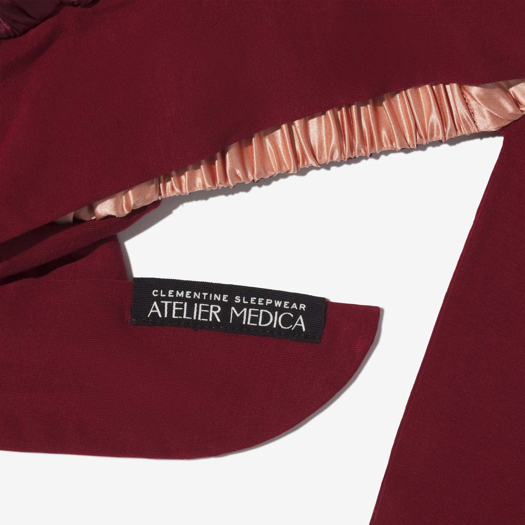 Maroon garment hem with sewn label reading 'CLEMENTINE SLEEPWEAR ATELIER MEDICA' and gathered peach lining.