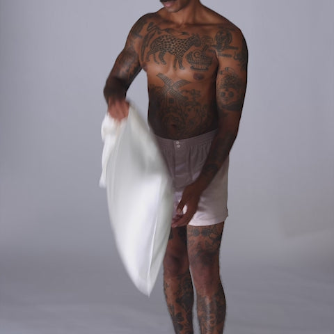 Tattooed man in pale boxer shorts holding a white pillowcase against gray studio background. - #color_pearl-white