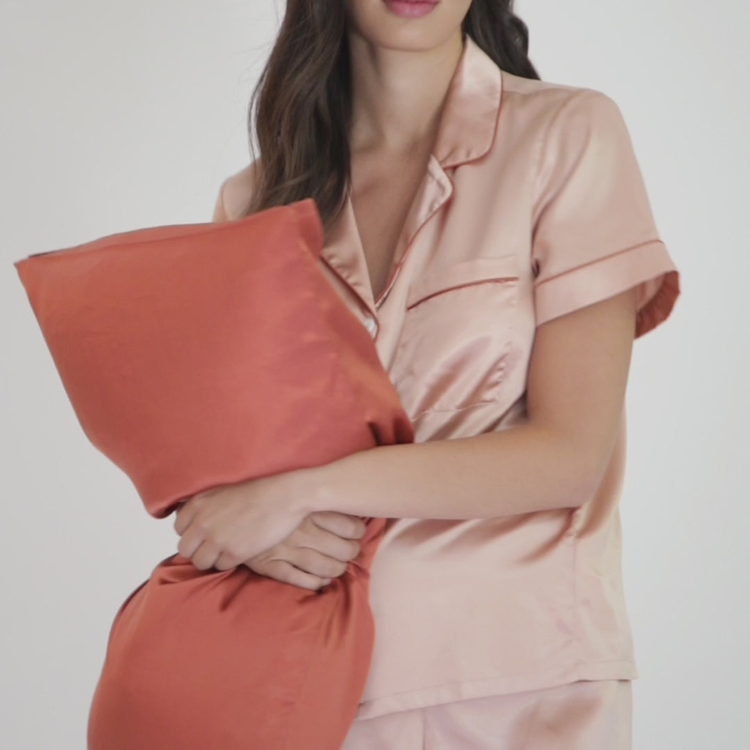 Woman in blush silk pajamas holding a rust-colored silk pillowcase#color_dusk