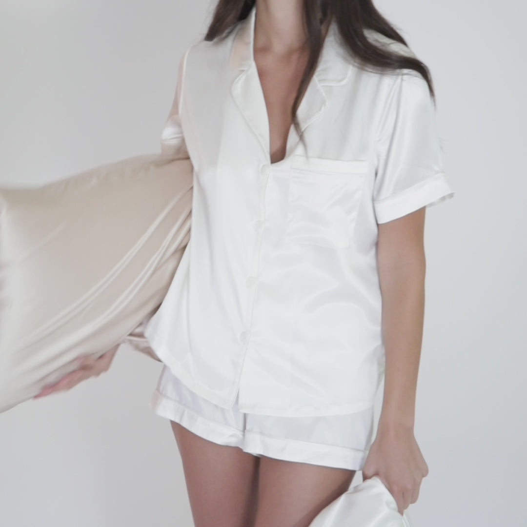 Woman in white silk pajamas holding a champagne-gold silk pillowcase.#color_champagne-gold