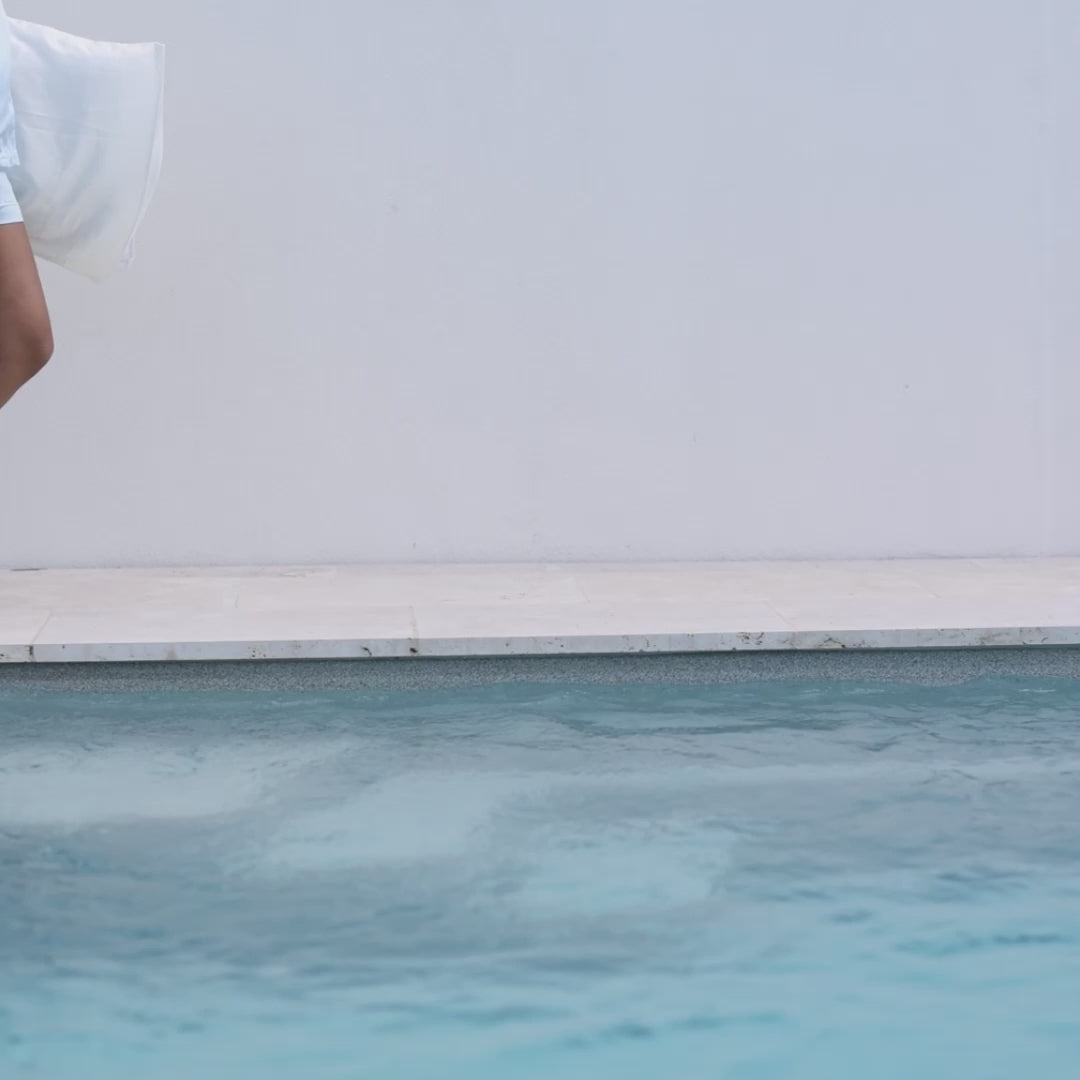 Person's legs mid-stride at pool edge holding a pearl-white silk pillowcase - walking with white pillowcase in silk#color_pearl-white