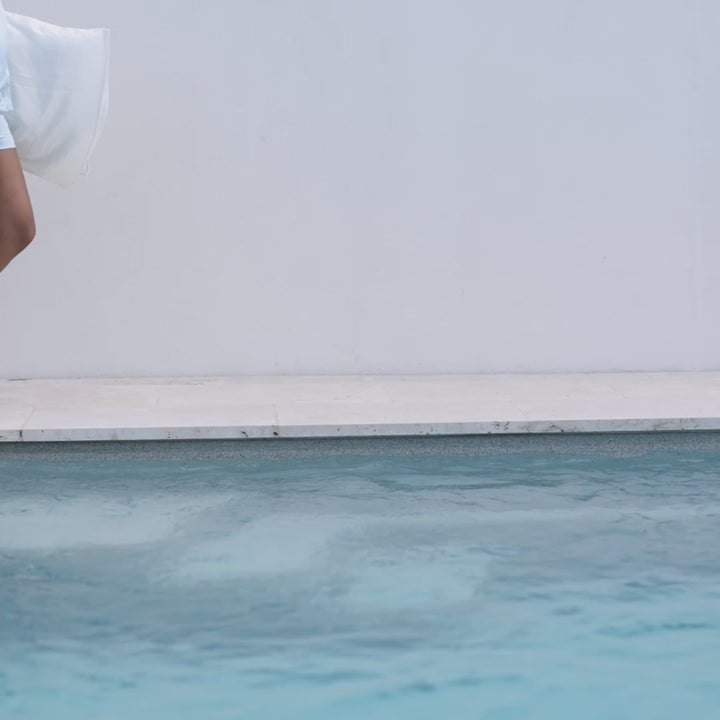 Person's legs mid-stride at pool edge holding a pearl-white silk pillowcase - walking with white pillowcase in silk#color_pearl-white