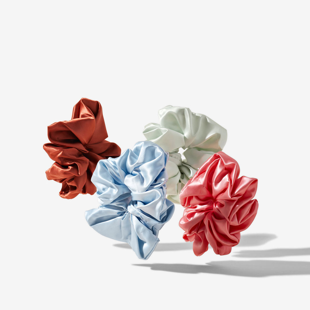 Four silk scrunchies in rust, pale blue, mint green, and coral on a white background