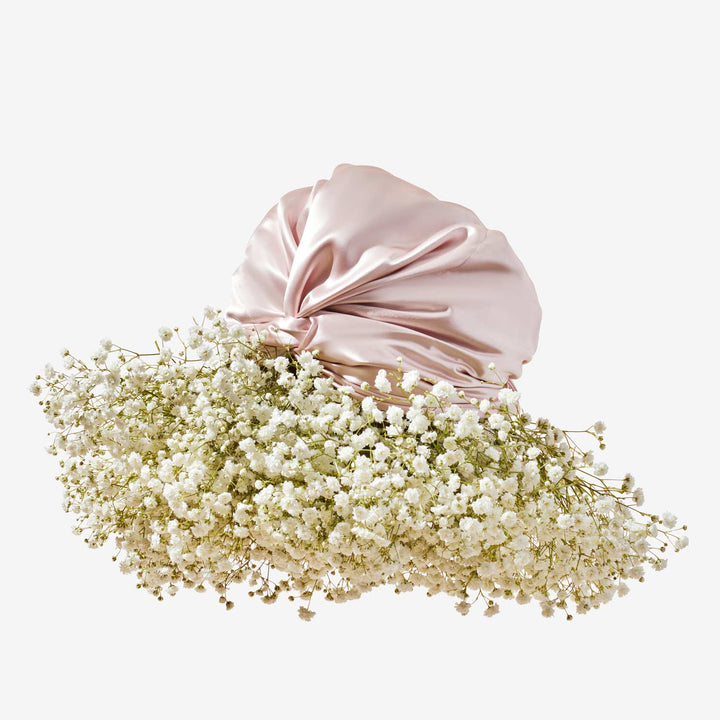 Pink silk turban resting on a large cluster of white baby's-breath flowers against a pale background.