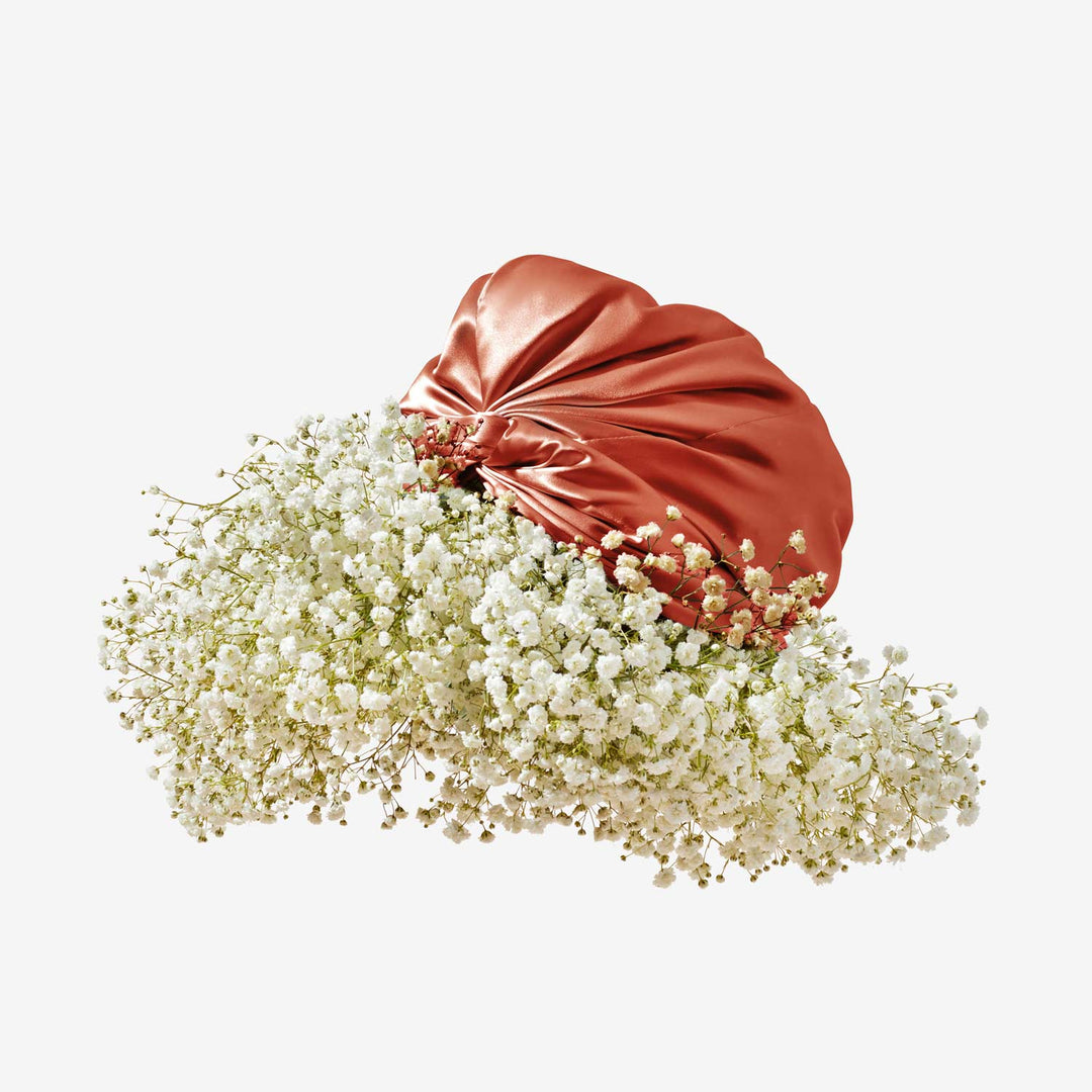 Red silk turban entwined with a cloud of white baby's breath flowers on a pale background.
