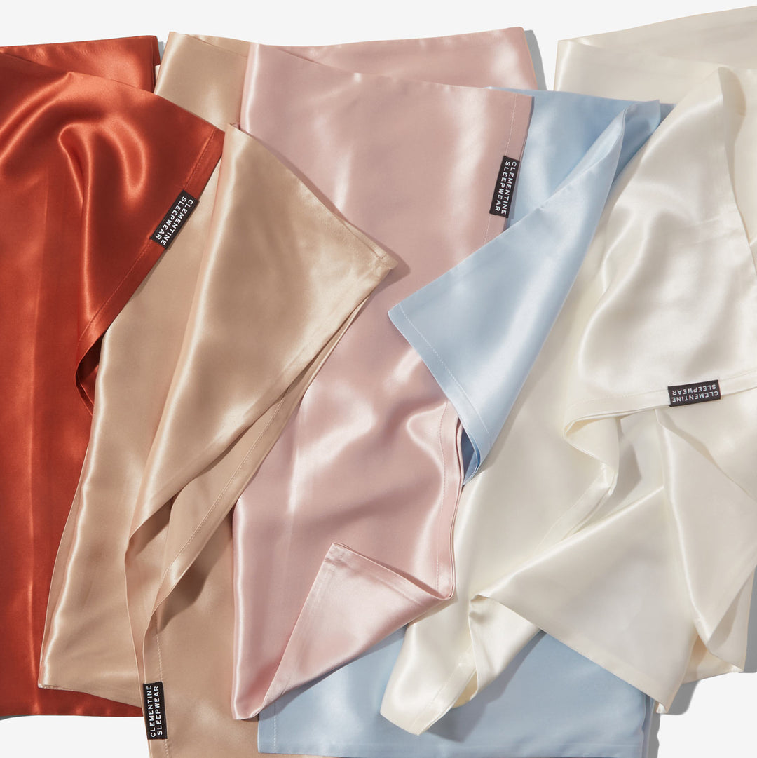 Silky silk pillowcases and fabric swatches in rust, beige, blush, blue, and ivory with tags reading CLEMENTINE SLEEPWEAR