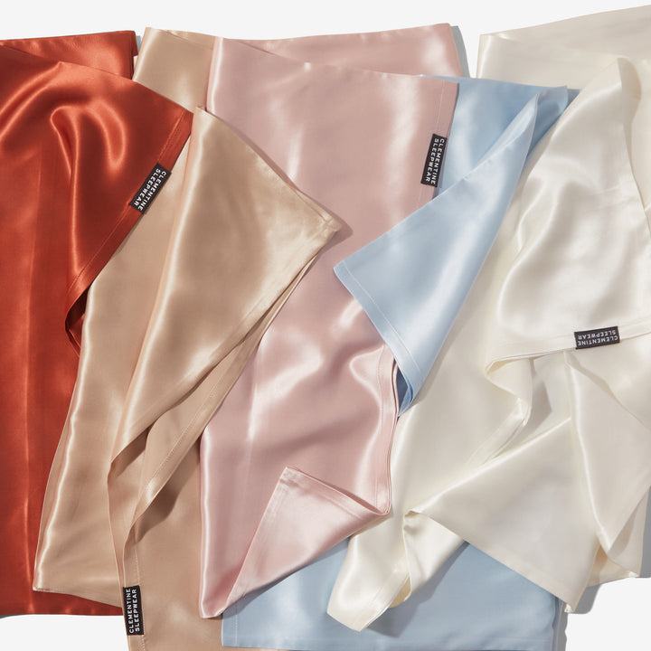 Silky silk pillowcases and fabric swatches in rust, beige, blush, blue, and ivory with tags reading CLEMENTINE SLEEPWEAR