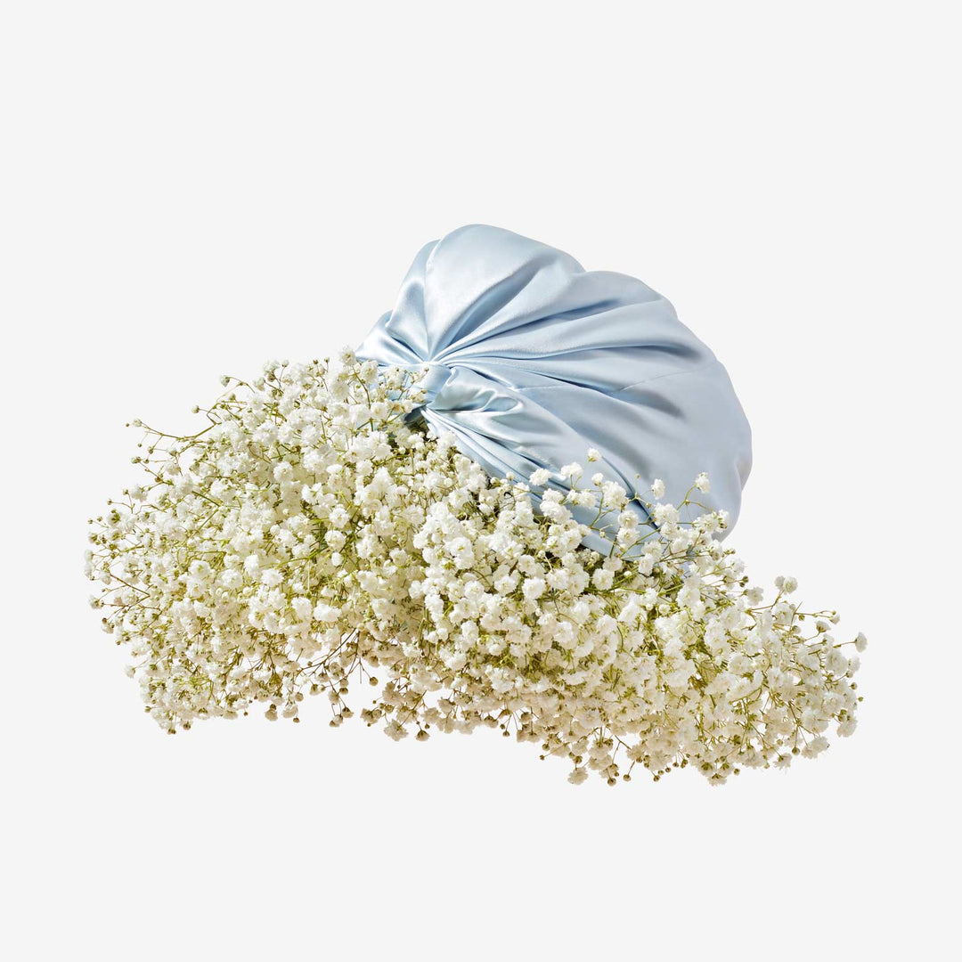 Pale blue silk turban cradling a cloud-like cluster of white baby's-breath flowers on a beige background.